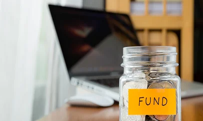 Coin jar labelled fund beside a laptop